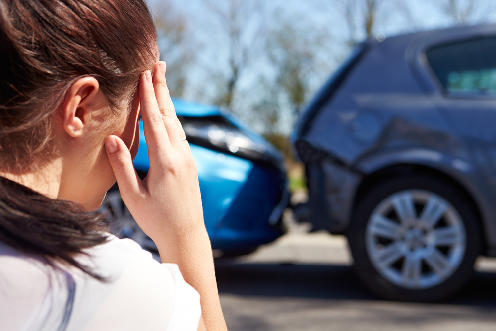 Stressed woman looking at her rear ended vehicle